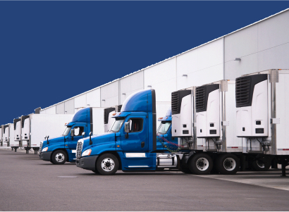 A day cab big rigs semi trucks with a reefer trailers stand near the gate of the warehouse next to other reefer trailers that are loaded and unloaded to deliver perishable and frozen food to consumers